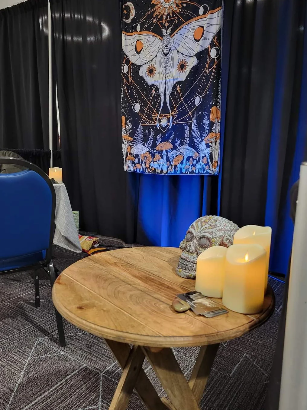 A round wooden reading table with candles, a sugar skull and a luna-moth tapestry.