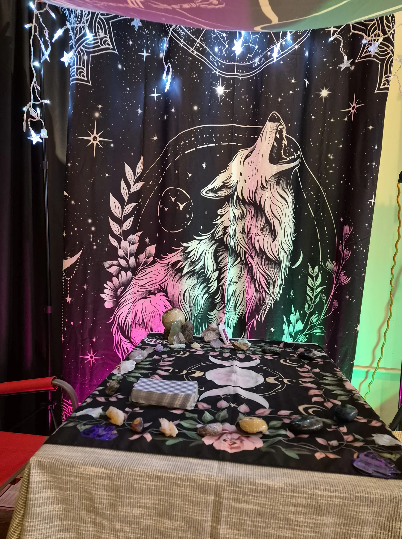 Crystal’s tarot table beneath a howling-wolf tapestry, lit pink and teal.